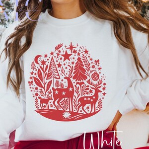 May include: White sweatshirt with a red Christmas design. The design features deer, trees, stars, and other festive elements. The word "White" is written in a script font at the bottom.