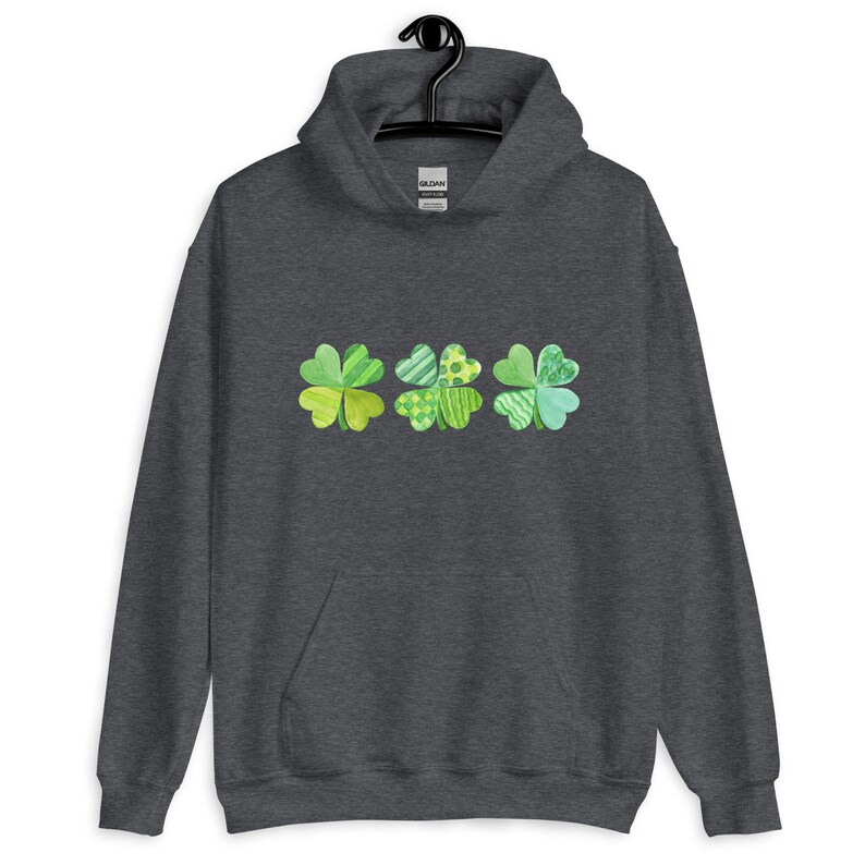 May include: A dark gray hoodie with a row of three green four-leaf clovers printed on the front. The clovers are made up of different green patterns.