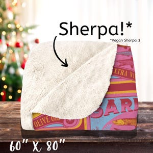 May include: A soft, plush blanket with a vintage-style sardine can design. The blanket is 60 inches by 80 inches and features a red, blue, and yellow color scheme. The text on the can reads "Olive Oil" and "Extra Virgin".