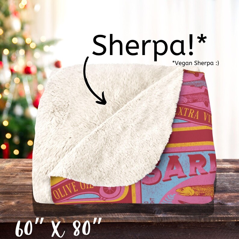 May include: A soft, plush blanket with a vintage-style sardine can design. The blanket is 60 inches by 80 inches and features a red, blue, and yellow color scheme. The text on the can reads "Olive Oil" and "Extra Virgin".