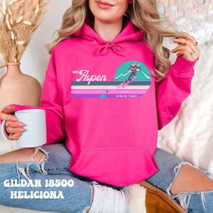 May include: A pink hoodie with a graphic print of a skier on a mountain with the text "Ski Aspen Since 1982".