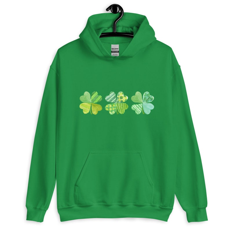 May include: Green hoodie with a row of three four-leaf clovers in shades of green and yellow. The clovers are made of patchwork fabric.