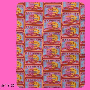 May include: A red and blue patterned fabric with a repeating design of sardine cans. Each can has a yellow label with the text "SARDINES IN EXTRA VIRGIN OLIVE OIL" and a picture of three sardines. The fabric is 60 inches by 80 inches.