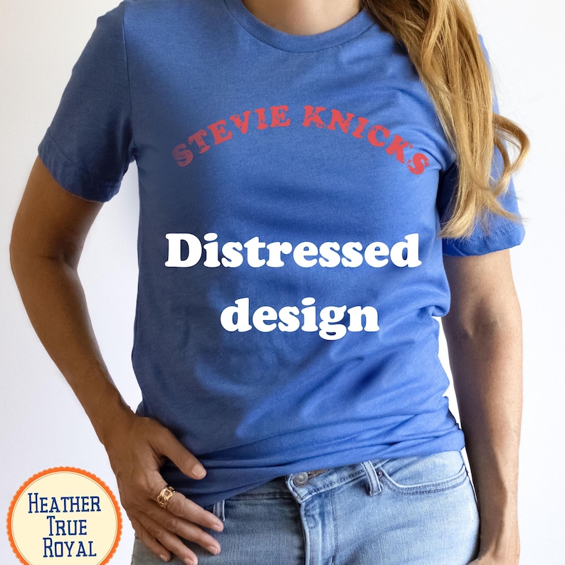 Puede incluir: Una camiseta de manga corta en color azul real jaspeado con el texto rojo STEVIE NICKS en fuente arqueada, y el texto blanco Distressed design centrado debajo. La prenda cuenta con un cuello redondo y un corte est&aacute;ndar de estilo casual.