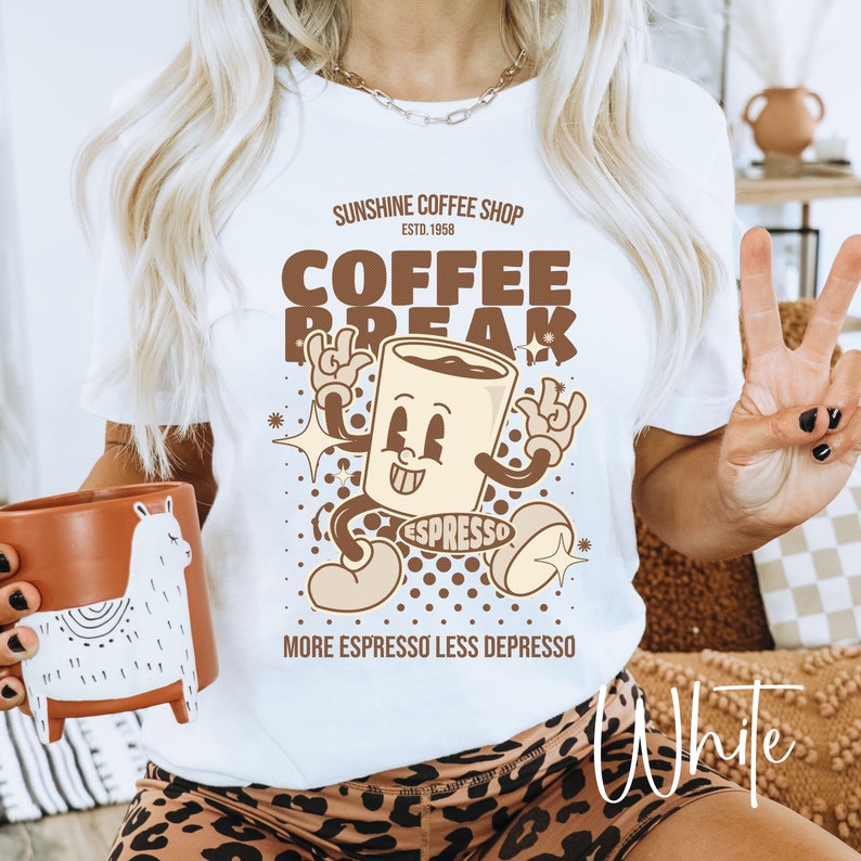 May include: White t-shirt with a brown cartoon coffee cup graphic. The graphic says "Sunshine Coffee Shop Est. 1958 Coffee Break" and "Espresso" on the cup. The text below the graphic says "More Espresso Less Depresso".