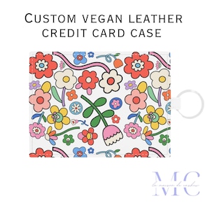 May include: A white vegan leather credit card case with a colorful floral pattern. The case has a small metal ring attached to the side.