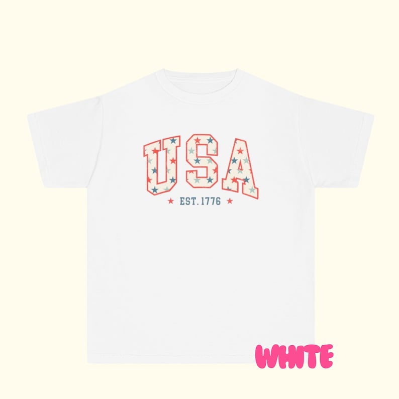 May include: White t-shirt with the word "USA" in a collegiate font, filled with a pattern of red, white, and blue stars. Below the word "USA" is the text "EST. 1776" with stars on either side. The word "WHITE" is written in pink.
