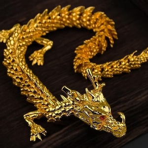 Puede incluir: Una figurita de dragón de color dorado con un ojo de piedra preciosa roja. El dragón está enroscado en un círculo con su cola en su boca.