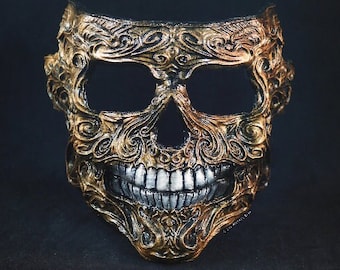 May include: A gold and black masquerade mask with a skull design. The mask has intricate details and a toothy grin.