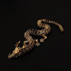 Puede incluir: Una figurita de dragón de color dorado con detalles intrincados, enroscada en una pose serpentina. Las escamas y las garras del dragón son visibles.