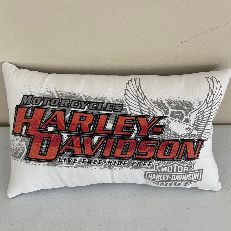 K&ouml;nnte beinhalten: Ein wei&szlig;es Kissen mit einem roten und grauen Harley-Davidson-Logo. Das Logo lautet "Motorcycles Harley-Davidson Live Free-Ride Free Motor Harley-Davidson Cycles".