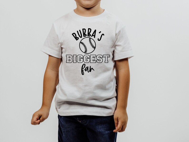 Peut inclure: T-shirt blanc avec du texte noir qui dit "Bubba's Biggest Fan" et un graphique de baseball.