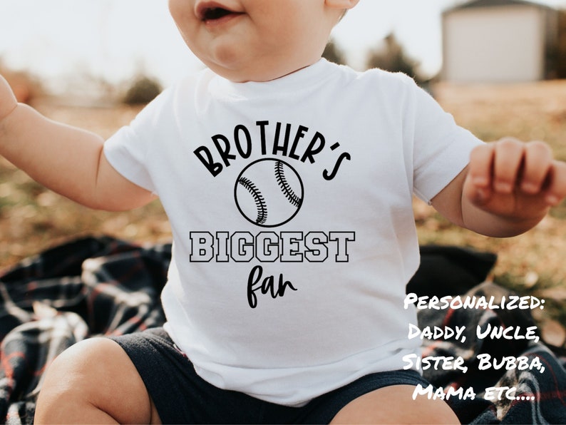 Peut inclure: Un body b&eacute;b&eacute; blanc avec un texte noir qui dit "Brother's Biggest Fan" avec un graphique de baseball. Le texte "Personnalis&eacute; : Papa, Oncle, S&oelig;ur, Bubba, Maman ETC..." est &eacute;crit en noir dans le coin inf&eacute;rieur droit du body b&eacute;b&eacute;.