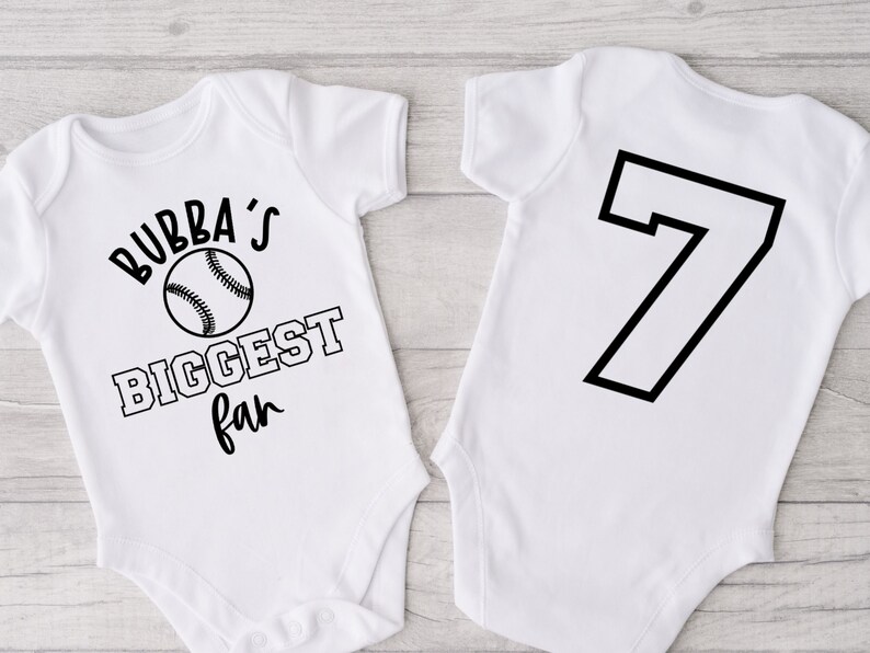 K&ouml;nnte beinhalten: Wei&szlig;er Baby-Strampler mit schwarzem Text "Bubba's Biggest Fan" und einem Baseball-Motiv. Die R&uuml;ckseite des Stramplers hat eine schwarze Nummer 7.