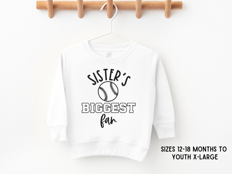 K&ouml;nnte beinhalten: Wei&szlig;er Langarm-Sweatshirt mit schwarzem Text, der "Sister's Biggest Fan" lautet, und einer Baseball-Grafik.