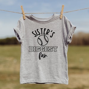 K&ouml;nnte beinhalten: Ein graues T-Shirt mit einem schwarzen Baseball-Motiv und dem Text "Sister's Biggest Fan".