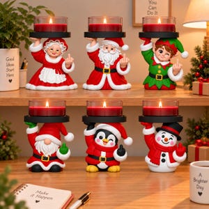 Op de afbeelding: Zes kerst-themahouders met mevrouw de Kerstman, de Kerstman, een elf, een kabouter, een pinguïn en een sneeuwpop. Elk figuur houdt een zwart rond plateau vast met een glazen houder en een rode kaars. De figuren maken een middelvingergebaar.