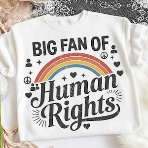Op de afbeelding: Wit T-shirt met de tekst "BIG FAN OF Human Rights" in zwart, boven een regenboogontwerp. Het ontwerp bevat harten, sterren en vredessymbolen. Een casual grafisch T-shirt.