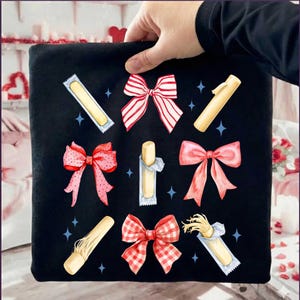 Könnte beinhalten: Schwarzer quadratischer Stoff mit Illustrationen von roten, rosa und weißen Schleifen sowie verpackten, hellfarbigen Stäbchen. Die Schleifen haben verschiedene Muster, darunter Streifen und Vichy. Blaue Sternakzente umgeben die Designs.