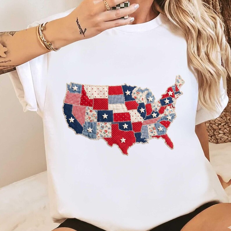 May include: White t-shirt featuring a patchwork design of the United States map. The map is composed of red, white, and blue fabric pieces with star accents. The shirt has short sleeves and a crew neck.