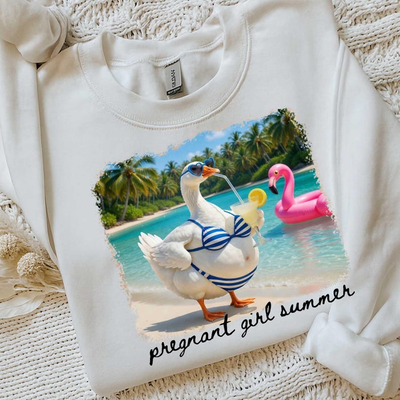 Pu&ograve; includere: Felpa bianca con una grafica di un'oca con occhiali da sole e un bikini a righe blu e bianche, che tiene in mano un cocktail su una spiaggia. Un galleggiante a forma di fenicottero rosa &egrave; sullo sfondo. Il testo "pregnant girl summer" &egrave; sotto.