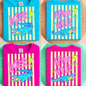 Puede incluir: Cuatro camisetas, dos en turquesa y dos en magenta, cada una con un diseño único. Los diseños presentan un cocodrilo de dibujos animados, texto y rayos. El texto en las camisetas turquesas dice "LATER" y "AFTER WHILE". Las camisetas magenta también tienen el mismo texto.