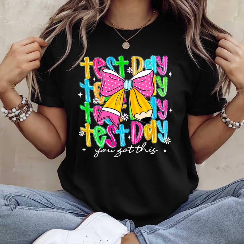 May include: Black t-shirt with a colorful graphic that says "Test Day" multiple times, with a pink polka-dot bow and a yellow pencil design. The text "you got this" is also included in the design.