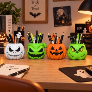 Puede incluir: Cuatro organizadores de escritorio con forma de calavera blanca, monstruo verde, calabaza naranja y criatura verde, cada uno lleno de varios bolígrafos y lápices, dispuestos en fila sobre una superficie de escritorio de madera.