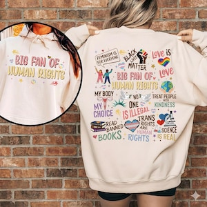 May include: A cream-colored sweatshirt with the text "BIG FAN OF HUMAN RIGHTS" on the front and a variety of colorful graphics and text on the back, including "Feminism is for Everyone", "Black Lives Matter", and "Trans Rights are Human Rights".