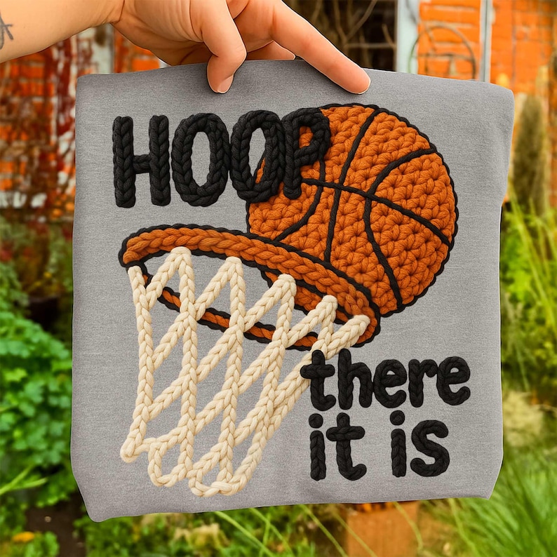 May include: A gray t-shirt featuring a basketball hoop design. The word "HOOP" is in black, the basketball is orange and black, and the net is white. The phrase "there it is" is in black.