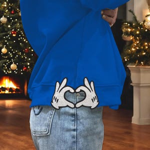 May include: A royal blue sweatshirt with a white glitter heart design made with two hands forming a heart shape.