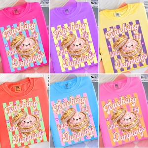 Puede incluir: Una colección de sudaderas de cuello redondo en varios colores, cada una con un gráfico de una empanadilla en una caja de joyas con el texto "Teaching my little Dumplings". Las sudaderas son de color rosa, morado, amarillo, naranja, azul y rosa claro.