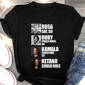 May include: Black t-shirt with portraits of Rosa Parks, Ruby Bridges, Kamala Harris, and Ketanji Brown Jackson. White text reads: "Rosa sat, so Ruby could walk, so Kamala could run, so Ketanji could rule."