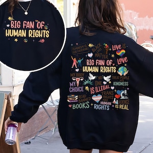 May include: Black sweatshirt with the text "BIG FAN OF HUMAN RIGHTS" in colorful lettering. The back of the sweatshirt features various graphics and phrases, including "Feminism is for Everyone," "Black Lives Matter," and "Love is."