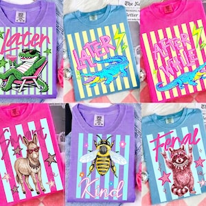 Puede incluir: Una colección de camisetas coloridas con varios diseños gráficos. Las camisetas presentan imágenes de un caimán, un burro, una abeja y un mapache, junto con las palabras "Later", "After While", "Smart", "Kind" y "Feral". Las camisetas tienen un fondo a rayas.