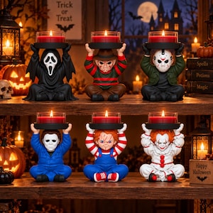 Peut inclure: Six bougeoirs représentant des personnages de films d'horreur disposés sur une étagère en bois. Chaque figurine est assise en tailleur et porte un plateau circulaire noir avec une bougie rouge au-dessus de sa tête. Les personnages incluent Ghostface, Freddy Krueger, Jason Voorhees, Michael Myers, Chucky et Pennywise.