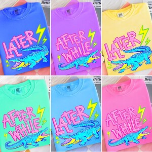 May include: A collection of crew neck sweatshirts in various colors, each featuring a cartoon alligator design with the text "LATER" or "AFTER WHILE" in pink, and a yellow lightning bolt. The alligator is blue with a yellow mouth.