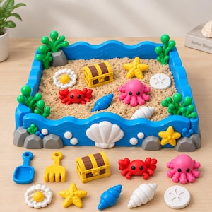 May include: A square blue sandbox with a wavy border containing beige sand, green plastic seaweed, and miniature figures including a yellow treasure chest, a red crab, a pink octopus, a yellow starfish, and white seashells.