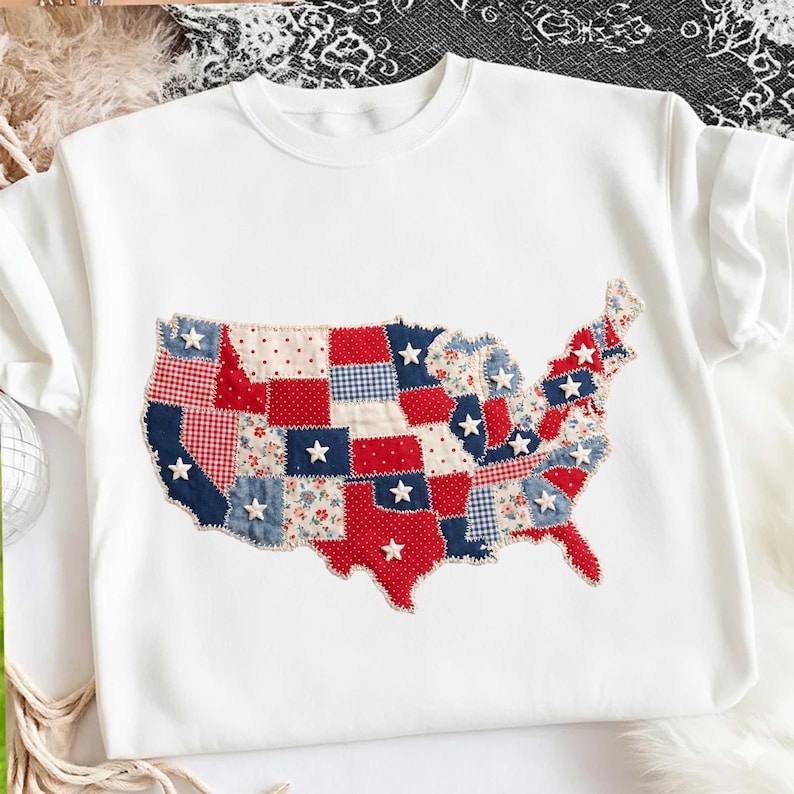 May include: White sweatshirt featuring a patchwork design of the United States map. The map is composed of red, white, and blue fabric squares with star accents. The design evokes a patriotic theme.