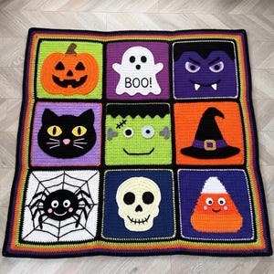 Könnte beinhalten: Eine quadratische Häkeldecke mit neun bunten Feldern mit Halloween-Motiven: ein orangefarbener Kürbis, ein weißes Gespenst mit dem Text BOO!, ein violetter Vampir, eine schwarze Katze, ein grünes Monster, ein schwarzer Hexenhut, eine Spinne, ein Totenkopf und ein Zuckermais.