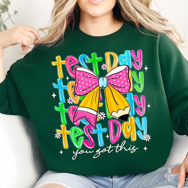 May include: Dark green sweatshirt with a colorful graphic. The graphic includes the words "Test Day" in multiple colors, a pink polka dot bow, and a yellow pencil. The phrase "you got this" is also included.