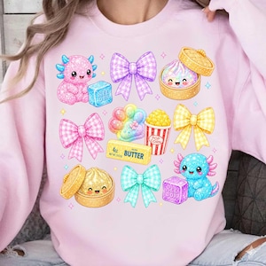 May include: A light pink sweatshirt featuring a colorful graphic print of two axolotls, four plaid bows in purple, pink, yellow, and teal, a dim sum basket, a popcorn bucket, and a stick of butter labeled 4oz BUTTER NET WT 113g.