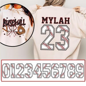 Puede incluir: Sudadera crema con temática de béisbol con la palabra "baseball" y un gráfico de bate, guante y lazo. La parte trasera presenta el nombre "MYLAH" sobre el número "23" en una fuente de béisbol. Se muestra un conjunto de números estilo béisbol debajo.