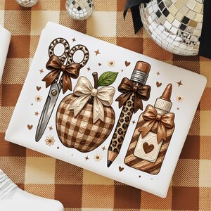 May include: A white rectangular item featuring a graphic print of school supplies including leopard print scissors with a brown bow, a plaid apple with a cream bow, a leopard print pencil with a brown bow, and a glue bottle with a brown bow and heart.
