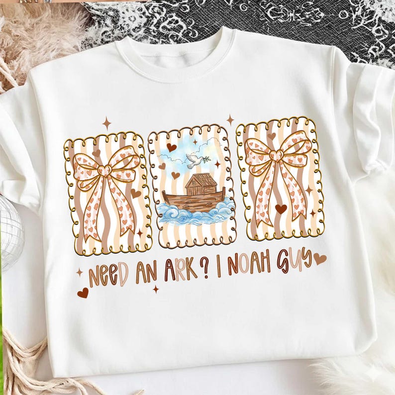 Puede incluir: Sudadera blanca con tres ilustraciones enmarcadas. Las ilustraciones incluyen un lazo, una paloma con una rama de olivo y el Arca de No&eacute;. El texto dice "Need an Ark? I Noah Guy". El dise&ntilde;o incorpora corazones y un fondo a rayas.
