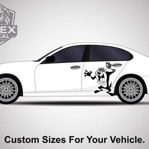 May include: A white car with a black Tazmanian Devil decal on the side. The decal is a black and white cartoon character. The text "Custom Sizes For Your Vehicle" is at the bottom. The Apex Decal logo is in the upper left corner.