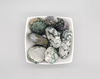 May include: A white bowl filled with moss agate tumbled stones. The stones are a mix of green, white, and gray with swirling patterns.