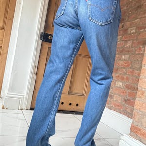 Könnte beinhalten: Blaue Jeans aus Denim mit klassischem Fünf-Taschen-Design. Die Jeans haben eine verwaschene Optik und einen Lederaufnäher auf der Rückseite. Das rote Levi's-Etikett ist auf der Gesäßtasche sichtbar. Ein zeitloser Kleiderschrank-Klassiker.