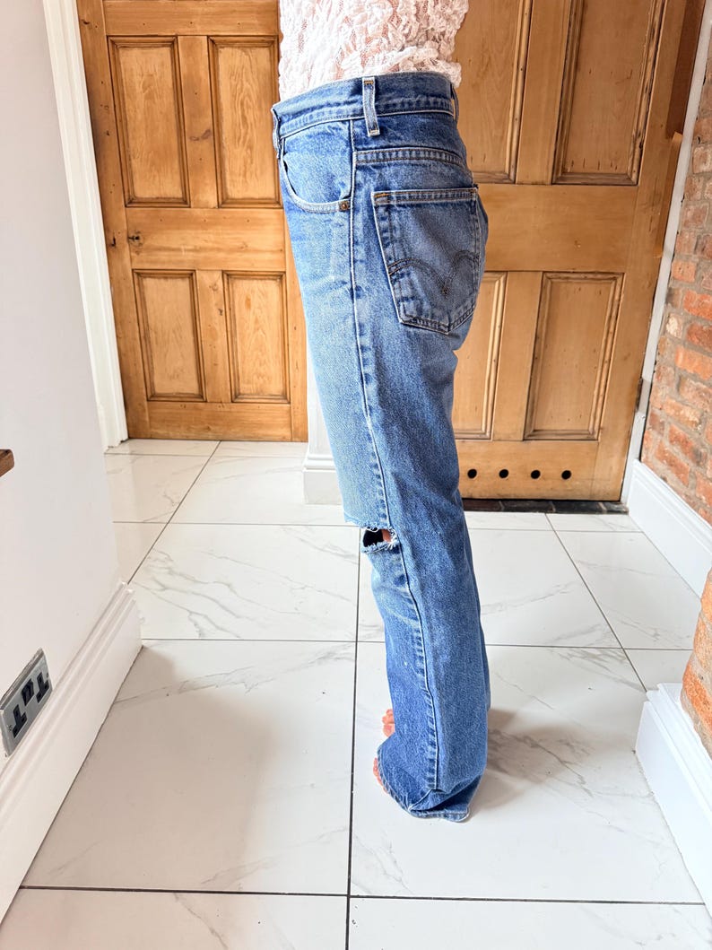 May include: Light blue denim jeans with a distressed knee detail. The jeans have a classic five-pocket design and a straight leg fit. The jeans are worn and have a faded appearance.
