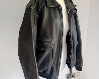 May include: A dark gray leather bomber jacket with a zip-up front, two front pockets, and a ribbed hem and cuffs. The jacket has a classic collar and shoulder epaulettes. The jacket is displayed on a mannequin.